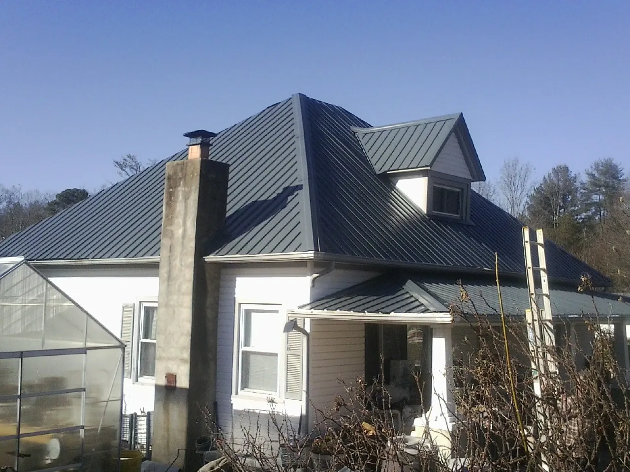 Dark blue standing seam metal roof on a white farmhouse with dormer — Slate & Tile Roof Repair by Roofing Brothers in Minong