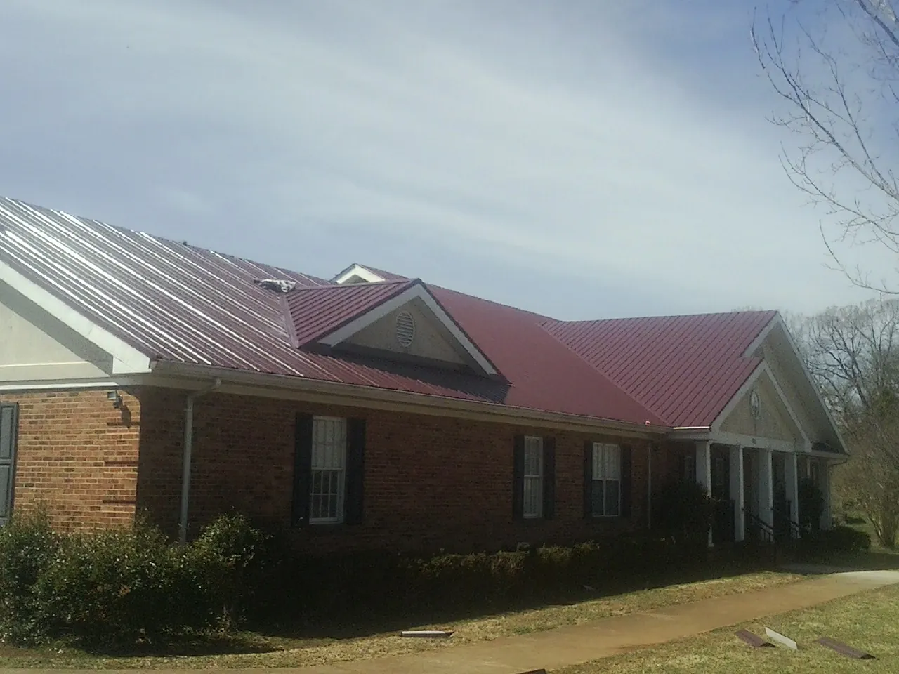 Red metal roof with gabled entries on a long brick building, from a Hail Damage Roof Repair job in Minong
