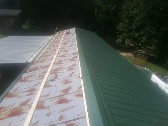 Old rusted panels beside newly installed green metal roofing — Wind Damage Roof Repair by Roofing Brothers in Minong