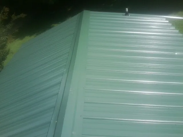 New green metal panels meeting at the ridge of a roof — Flat Roof Repair work by our crew in Minong