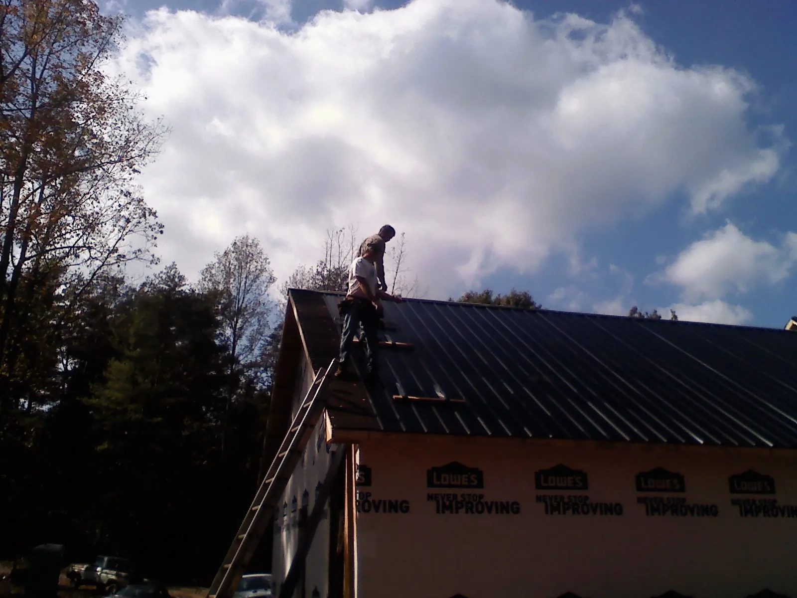 Roofer fastening dark metal panels high against a cloudy sky, from a Roof Inspection job in Minong