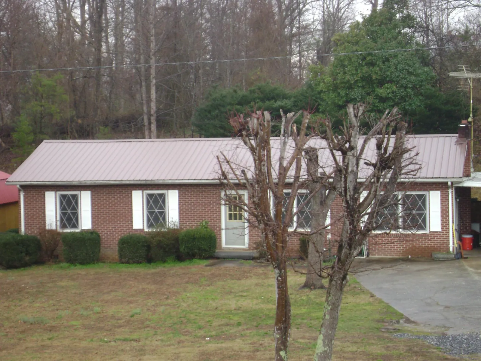 Mauve metal roof on a brick ranch home behind bare trees in Minong