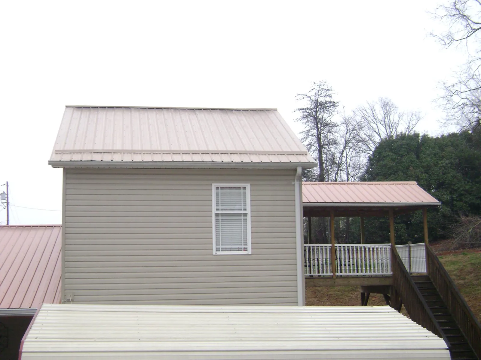Tan metal roofs on a two story addition and attached porch, from a Roof Replacement job in Minong